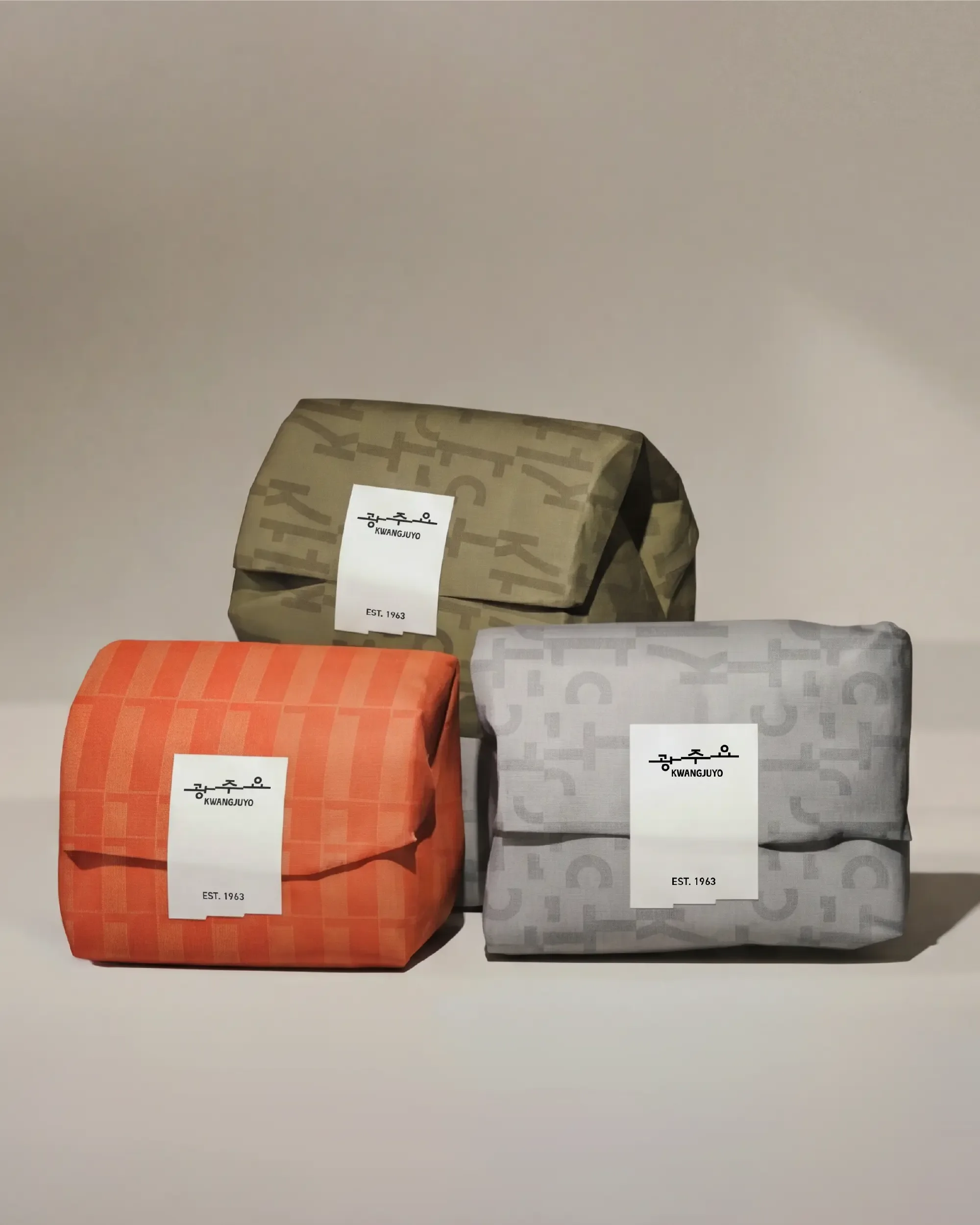 Three wrapped gift packages in orange, olive green, and grey patterned paper sealed with Kwangjuyo white brand stickers.