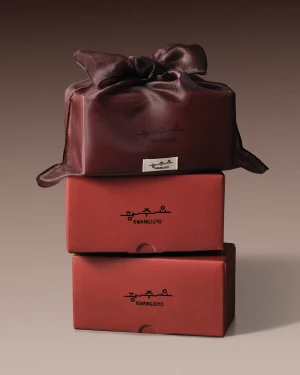 Stack of Kwangjuyo branded terracotta red gift boxes topped with a brown satin fabric wrap tied in a knot against a neutral background.