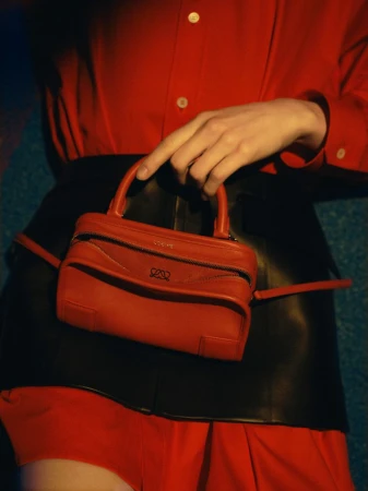 Model wearing a bright red button-up shirt and black leather skirt holding a small red leather handbag with a top handle.