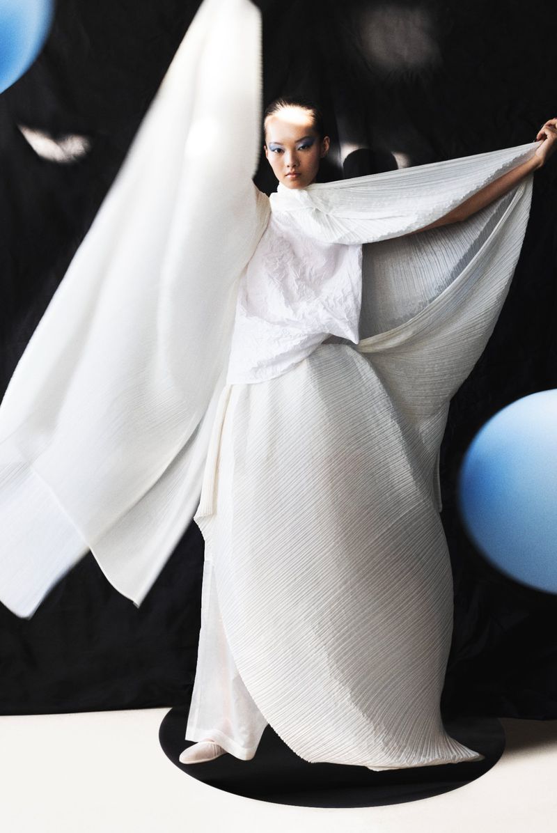 Woman in flowing white attire strikes a pose against a backdrop of black with light blue sphere. Fashion, fabric, style and elegance.