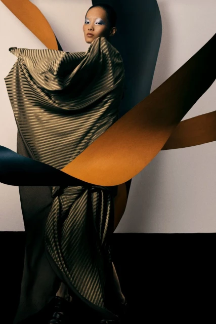 Asian female model in a gold striped gown poses against a gradient paper background, showcasing fashion and studio photography.
