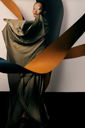 Asian female model in a gold striped gown poses against a gradient paper background, showcasing fashion and studio photography.