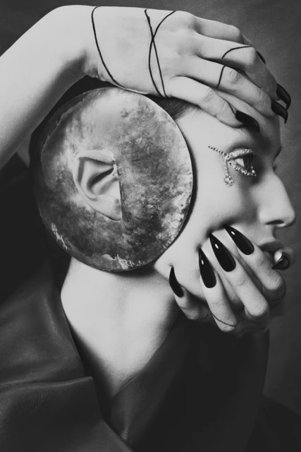 Artistic portrait of woman with long black nails and ear sculpture, adorned with jewels, in black and white, creative fashion beauty.