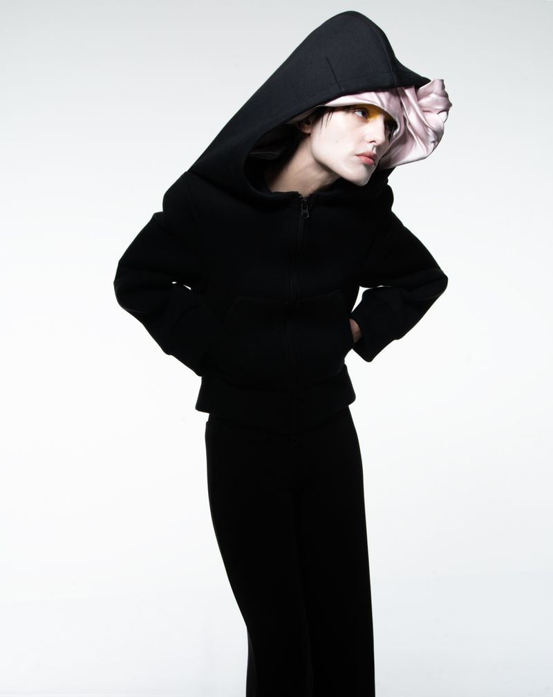 Fashion shot of a model wearing a black hooded top with a pink floral lining, complemented by a black skirt against a white backdrop.