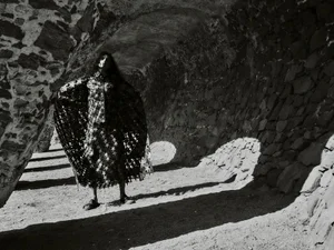 Model standing inside a stone archway wearing a dark patterned cape for Harper's Bazaar España.