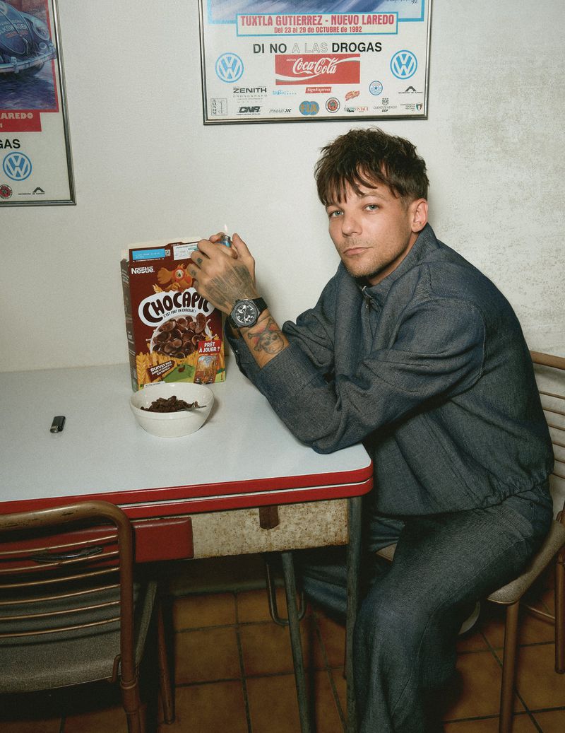 Louis Tomlinson sitting at a retro table holding a lighter next to a bowl and box of Chocapic cereal.