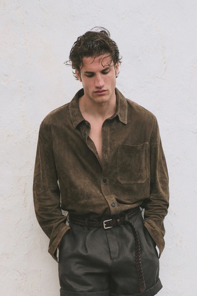 Model in olive green suede shirt and dark trousers against textured white wall for Massimo Dutti Static Matter SS26.