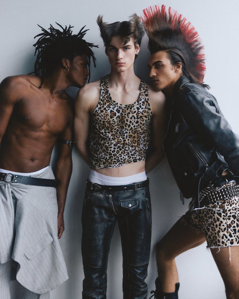 Three male models with punk-inspired hairstyles, leopard print, and leather garments pose against a plain studio background.