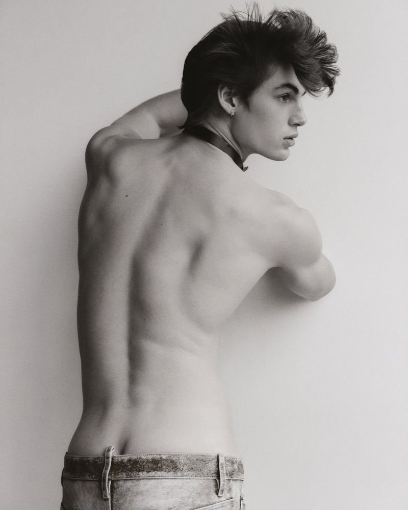 Black and white portrait of male model Finn Farrell shirtless from behind in low-rise jeans against a studio backdrop.
