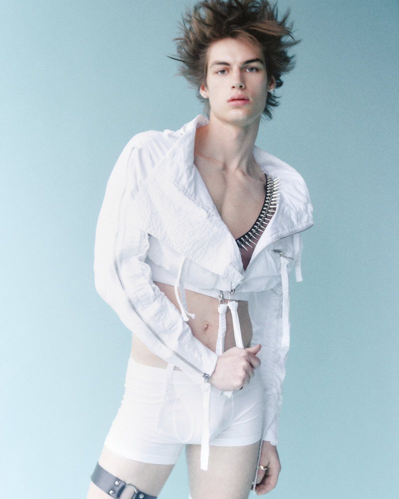 Model Finn Farrell wearing a cropped white jacket and white shorts against a soft blue backdrop for Man About Town.