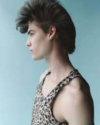 Profile portrait of a man with voluminous styled hair wearing a leopard print tank top against a blue background.