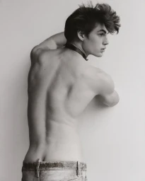 Black and white portrait of male model Finn Farrell shirtless from behind in low-rise jeans against a studio backdrop.