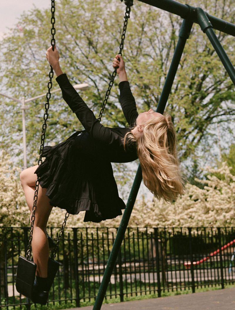 Young woman in a black dress on a swing set. Fair-skinned woman with blonde hair smiling outdoors on a sunny day at the playground.