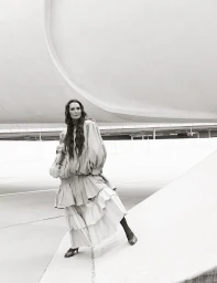 Brooke Shields posing in a voluminous layered tiered dress against curved modern architecture in black and white.