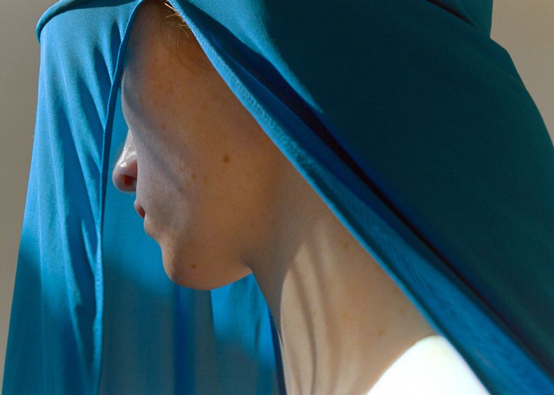 Close-up profile of a model draped in vibrant turquoise fabric with direct light casting shadows across the neck.