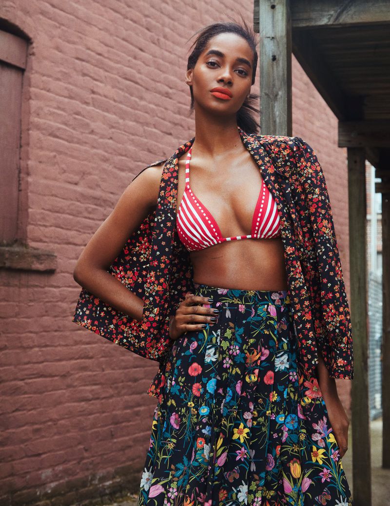 Model Tami Williams wearing a red striped bikini top with a floral print jacket and skirt beside a brick wall.