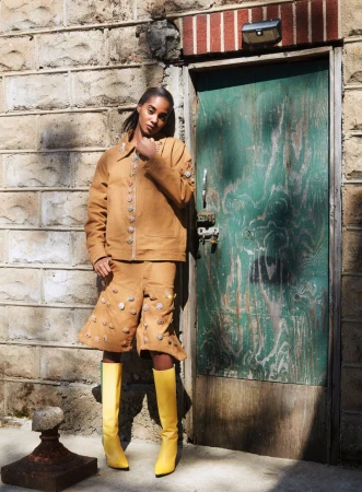 Model Tami Williams wearing tan jacket and yellow boots standing by a green door in Nataal Magazine editorial