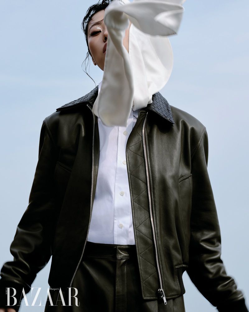 Model Heejung Park wearing a dark leather jacket and crisp white collared shirt against a pale sky for Harper's Bazaar Korea.