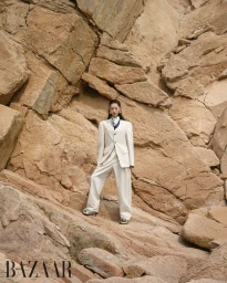 Model Heejung Park standing on a rugged rocky slope wearing an oversized cream tailored suit for Harper's Bazaar Korea.