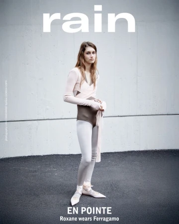 A fashion editorial shot with a woman wearing a leotard, tights, and ballet slippers, posing against a neutral urban backdrop. The magazine name 'rain' is visible.