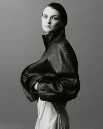 Monochrome portrait of a woman wearing a leather jacket and light-colored skirt against a neutral backdrop in a studio setting.