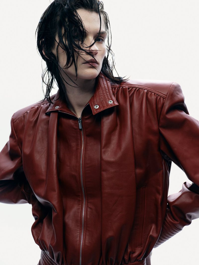 Lara Mullen wearing an oversized reddish brown leather bomber jacket with wet styled hair against a white seamless background.
