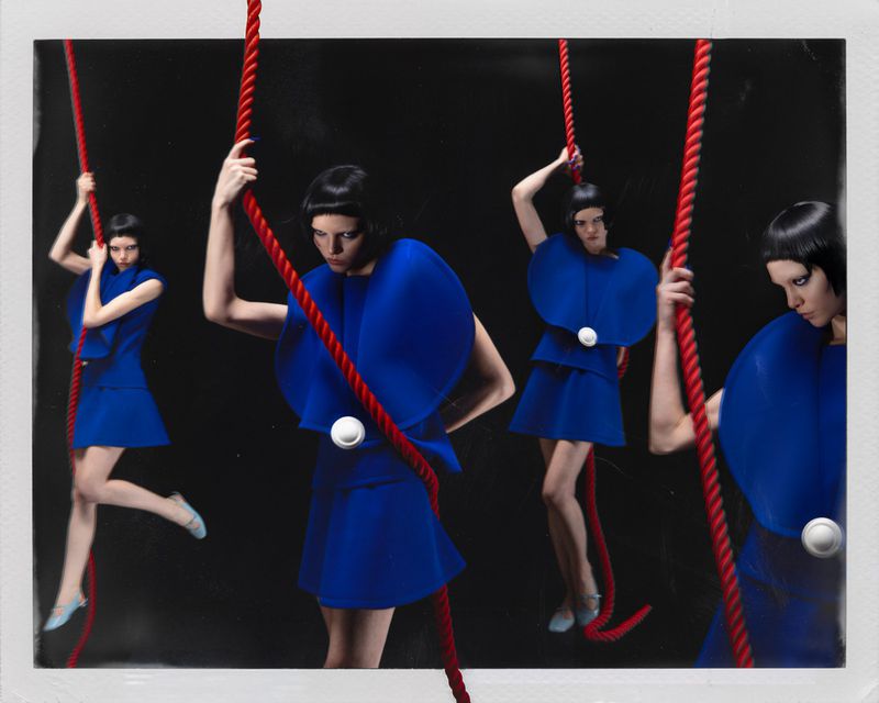Models with dark bob haircuts pose in cobalt blue sculptural mini dresses holding thick red ropes against a black studio background.