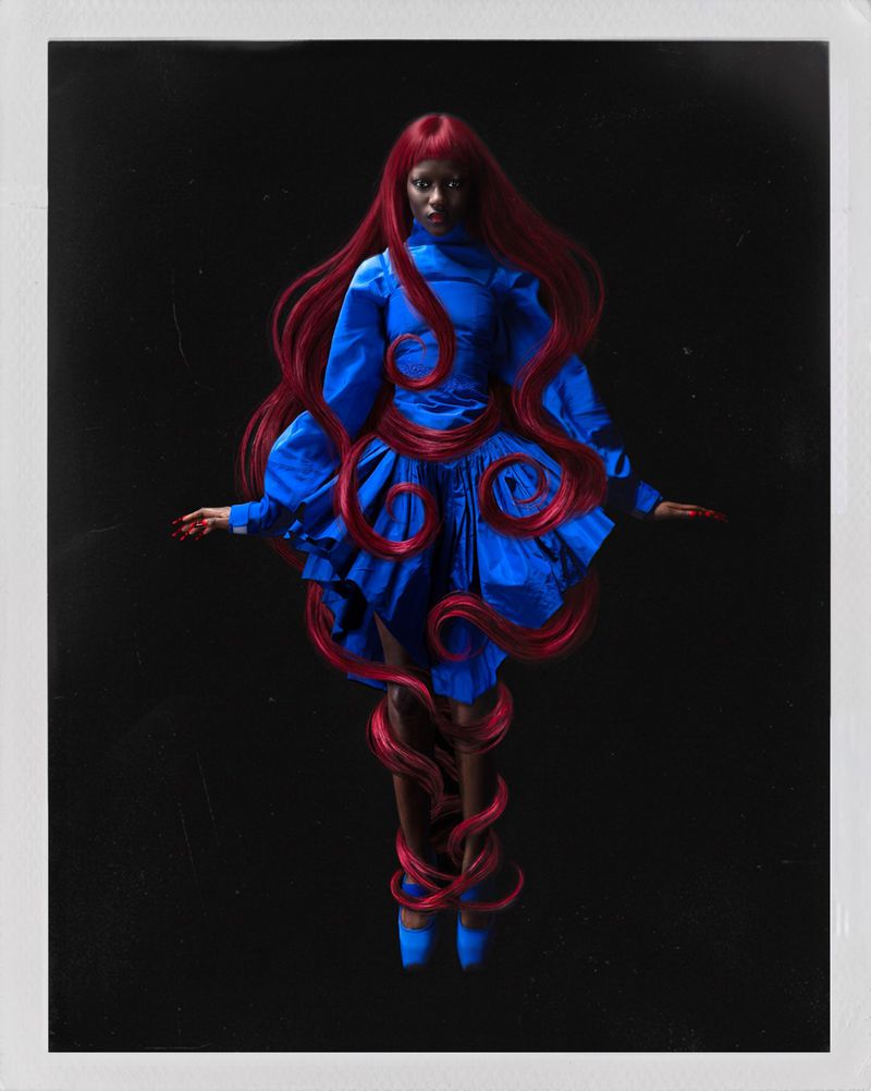 Model with long red hair wearing a blue dress against a dark background for Numero Netherlands by Valentin Fabre.