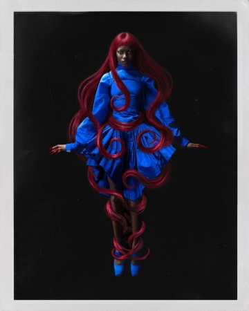 Model with long red hair wearing a blue dress against a dark background for Numero Netherlands by Valentin Fabre.