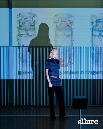 Model Minji Lee in a short-sleeved navy shirt and dark trousers posing before projected technical diagrams for Allure Korea.