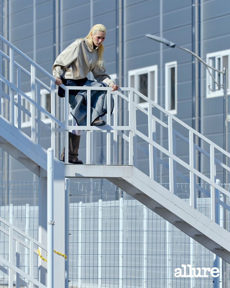 Model Minji Lee in a beige pullover and wide-leg trousers posing on a white metal outdoor staircase for Allure Korea.