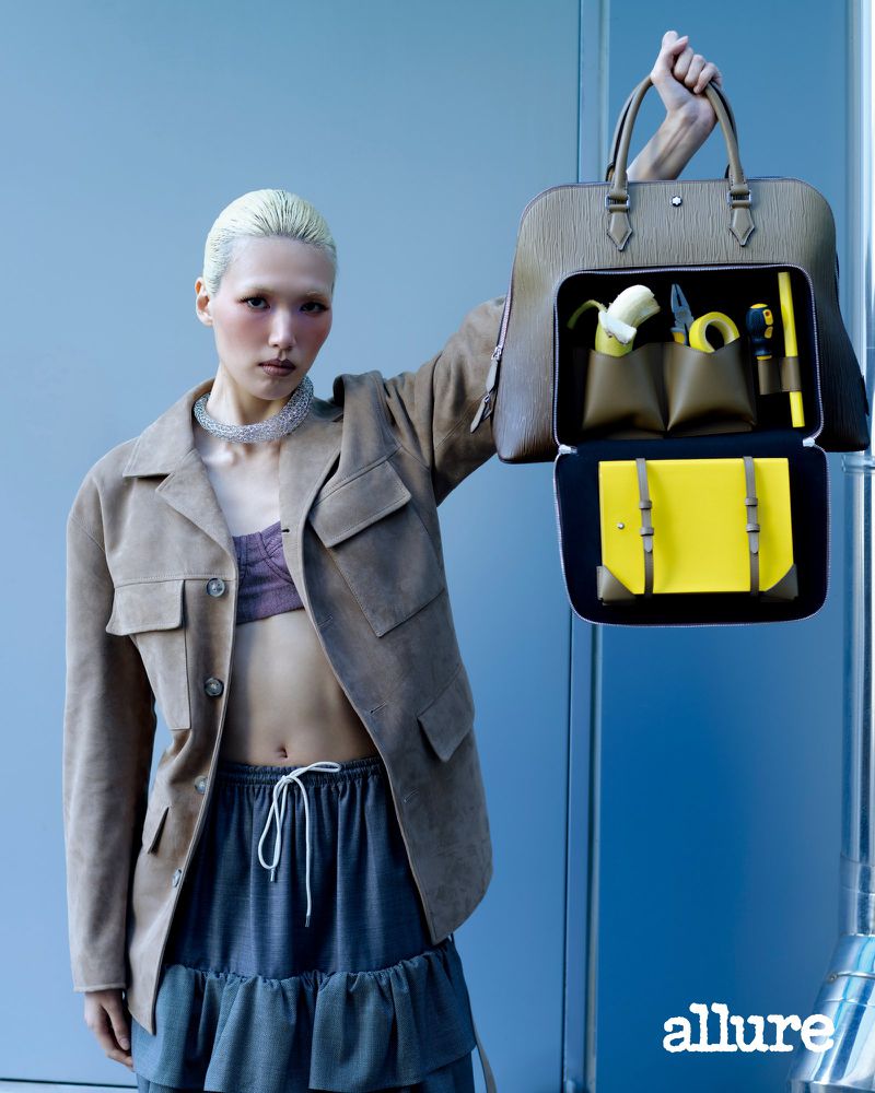 Model Minji Lee holds an open leather briefcase packed with yellow tools and a banana against a blue wall for Allure Korea.