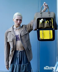 Model Minji Lee holds an open leather briefcase packed with yellow tools and a banana against a blue wall for Allure Korea.