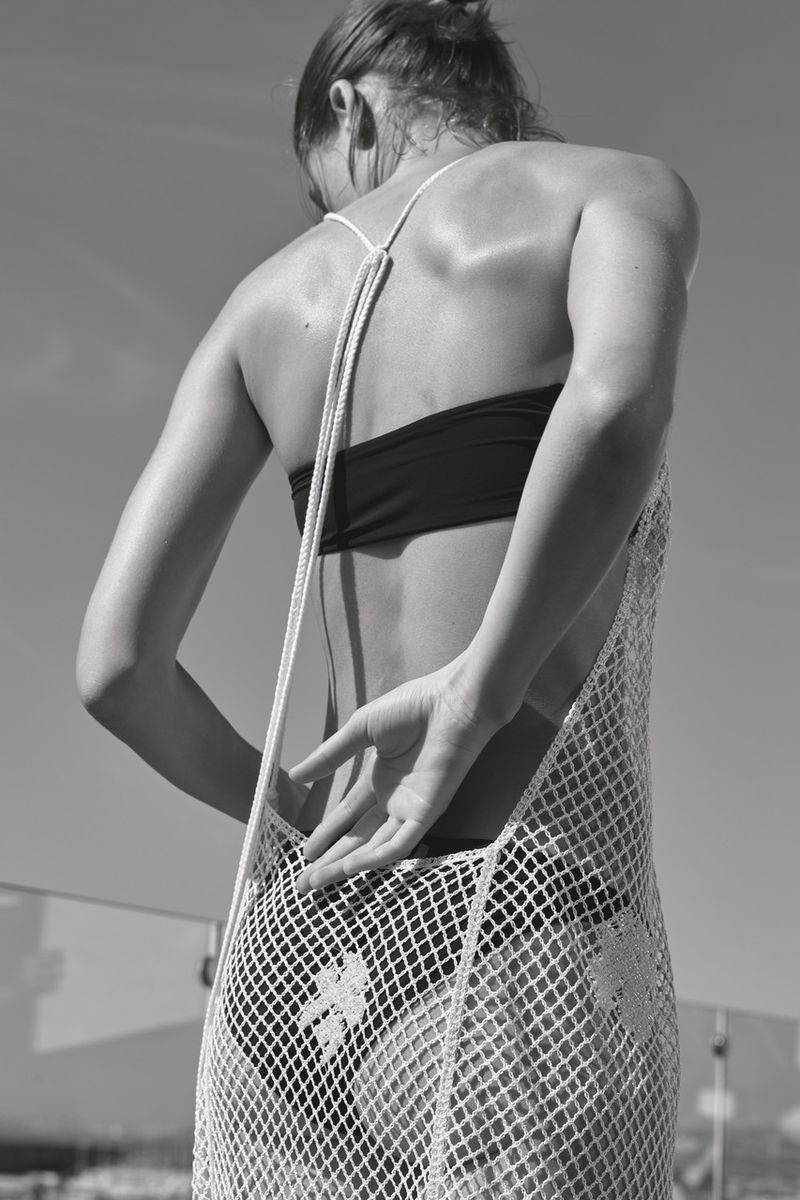 Black and white shot of model Bonnie Panasenko from behind wearing a black bikini and white crochet open-back dress.