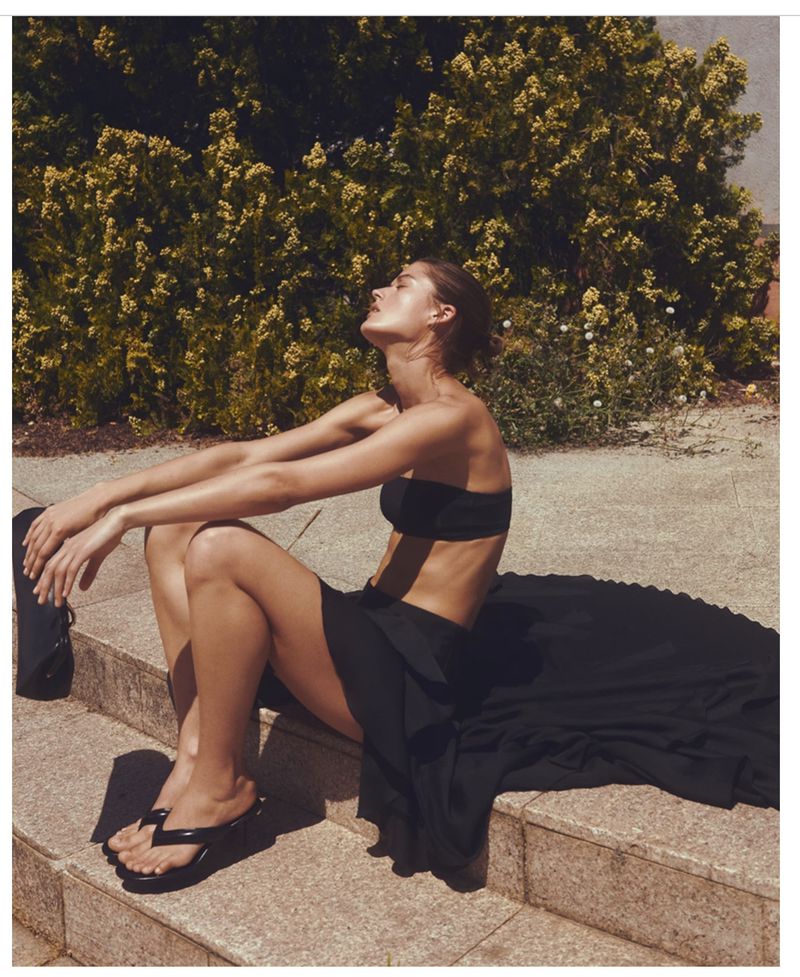 Model wearing a black strapless top and long skirt seated outdoors against foliage for H&M Du matin au soir project.