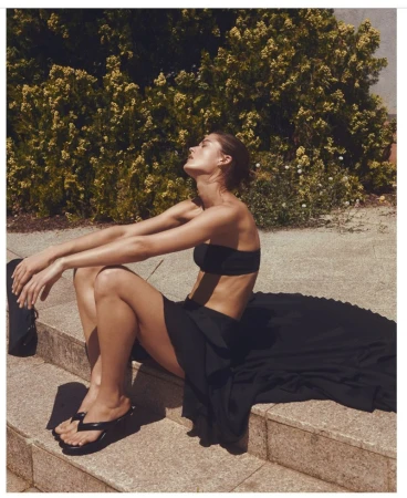 Model wearing a black strapless top and long skirt seated outdoors against foliage for H&M Du matin au soir project.