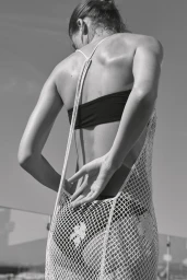 Black and white shot of model Bonnie Panasenko from behind wearing a black bikini and white crochet open-back dress.