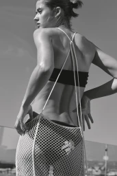 Model Bonnie Panasenko viewed from behind wearing a white open-weave crochet dress over dark swimwear in bright daylight.