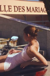 Model in a pink minidress resting on a scooter outdoors in front of a building exterior with text signage