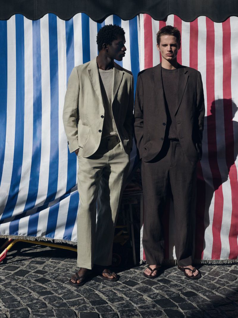 Two male models posing in lightweight tailored linen suits and flip-flops against blue and red striped fabric backdrops.