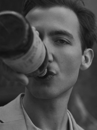 Monochrome close-up of a man in a tailored jacket drinking directly from a glass bottle.