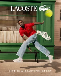 Man leaping mid-air wearing a red polo shirt, wide-leg jeans, and white sneakers outside a green storefront near a flying tennis ball.