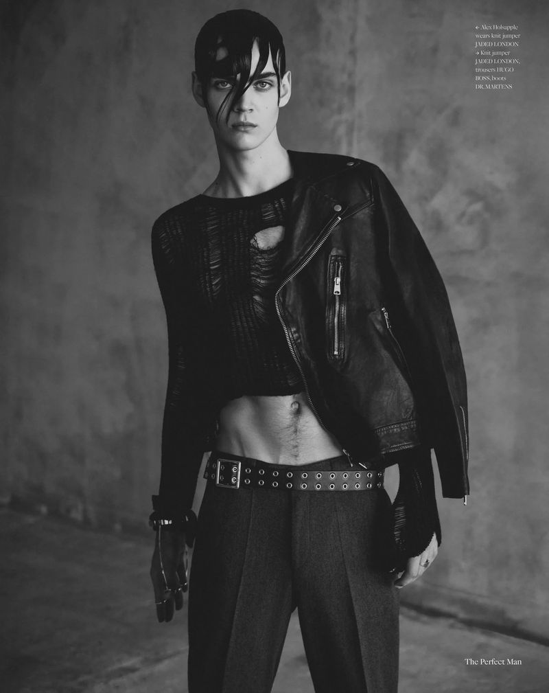 Male model with wet hair wearing a cropped distressed knit, leather jacket over one shoulder, and studded belt against a studio backdrop.