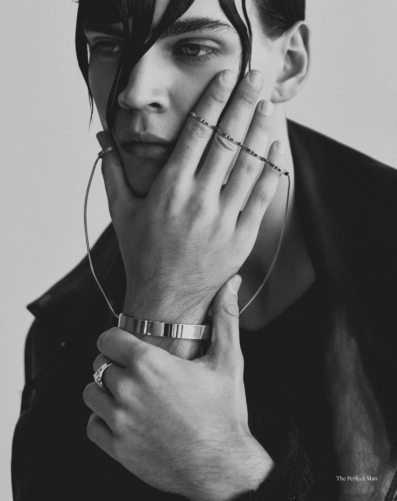 Black and white portrait of a man with wet hair resting his hand on his face while wearing metallic rings and wire jewelry.