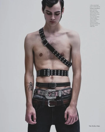 Shirtless male model wearing multiple black studded and western belts across his chest and waist against a grey studio backdrop.