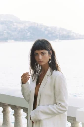 Model with dark hair wearing an off-white blazer against an open-air coastal background by Justin Woo for Sir The Label Spring project