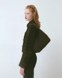Model in chocolate wool jacket carrying a matching shoulder bag against a plain white background