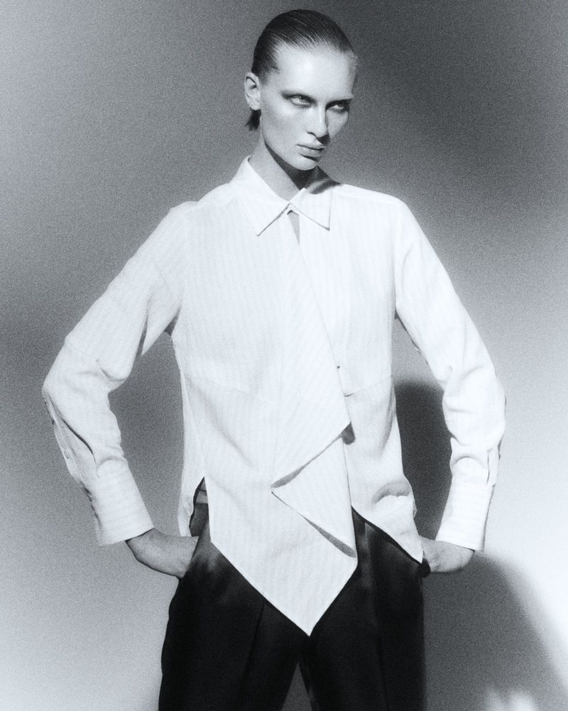 Fashion model Yanita in an asymmetric white collared shirt and black trousers against a studio backdrop for L'Officiel Chile.