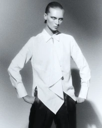 Fashion model Yanita in an asymmetric white collared shirt and black trousers against a studio backdrop for L'Officiel Chile.