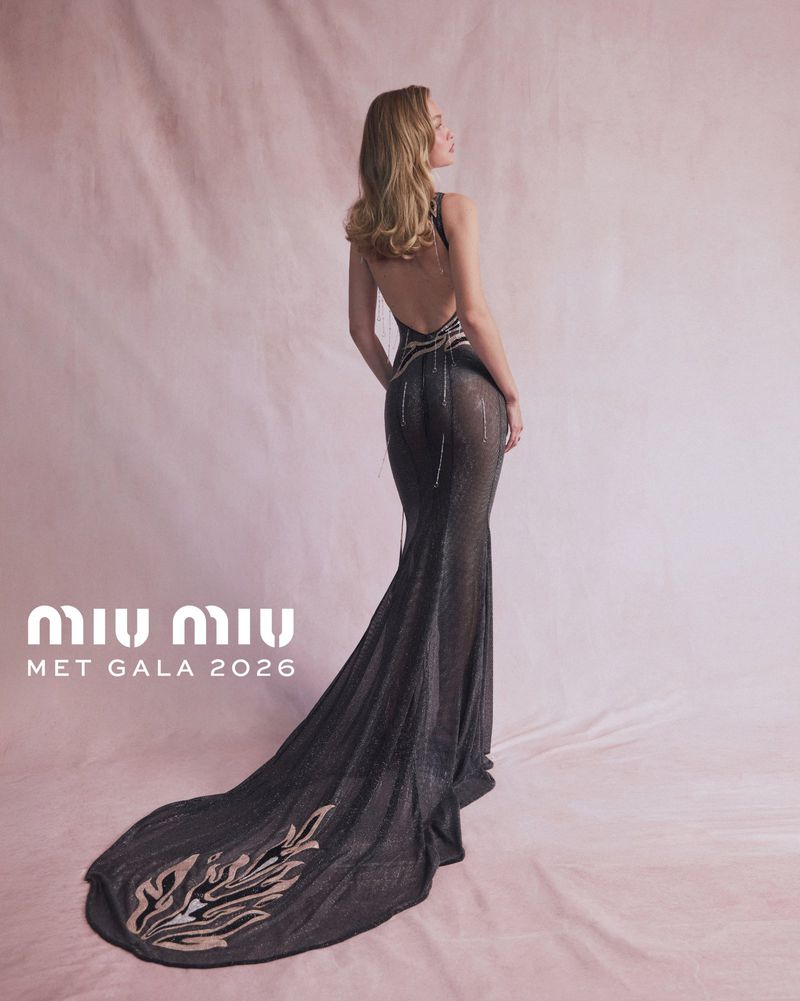 Model Gigi Hadid in a backless black evening gown with an embroidered train against a soft pink backdrop for Miu Miu.